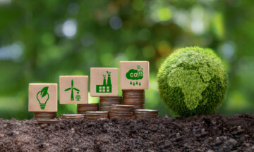 Carbon credit and CO2 emission reduction concept. Wooden cubes with CO2 icon on stack of silver coins and green globe with world map. Tax credits for enterprises to stop global warming process.
